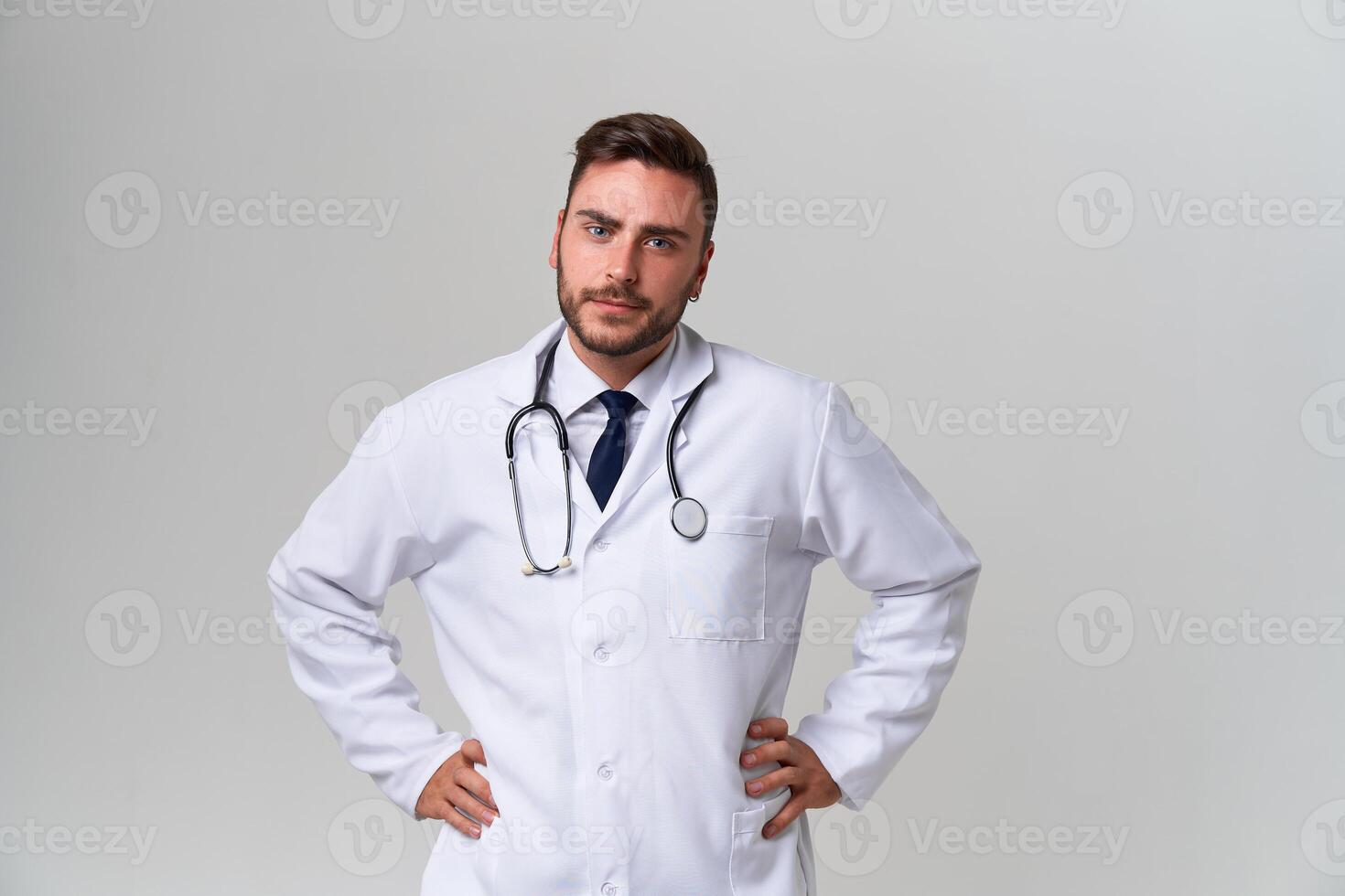 Young handsome modern doctor in a white medical gown stands in the studio on a white background. Student trainee of a medical university. photo