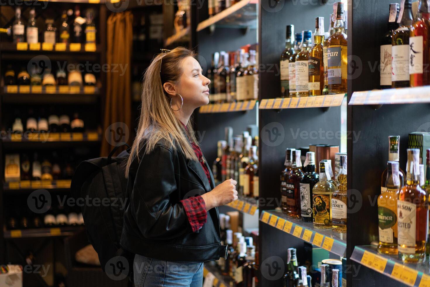 Ukraine. Kharkov Ocotber 2019 Young beautiful caucasian girl in a liquor store does not look at a shelf with bottles of whiskey. photo