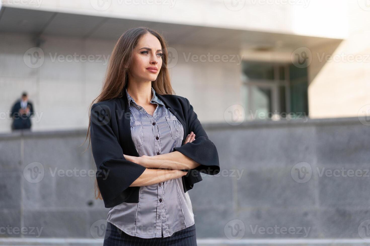 Business woman with long hair dressed black jacket standing outdoor near corporate office building hands folded photo