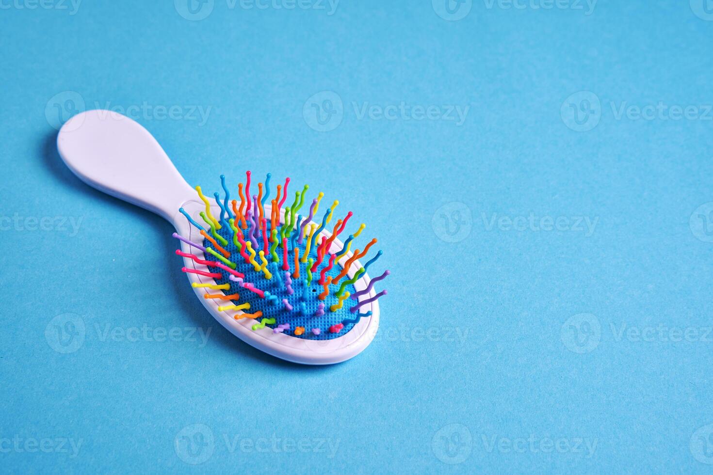 Funny baby comb with multi-colored plastic wavy bristles lies on a blue background. photo