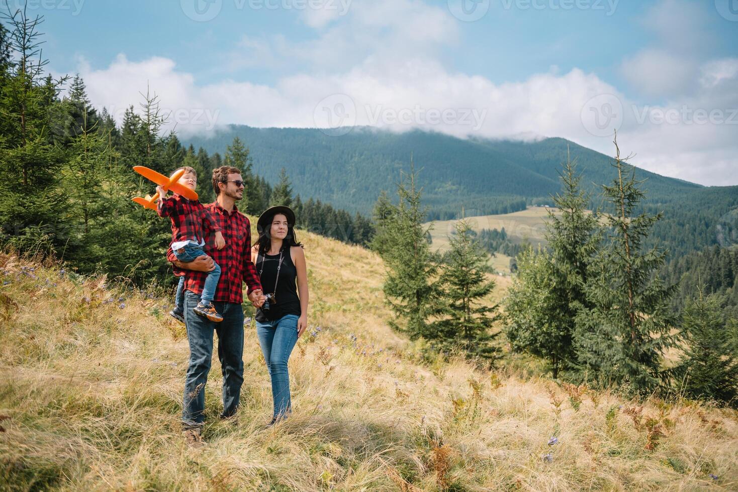 family walk on the field near the mountains in sunny day yellow grass father mother son holding hands on the sunset. photo