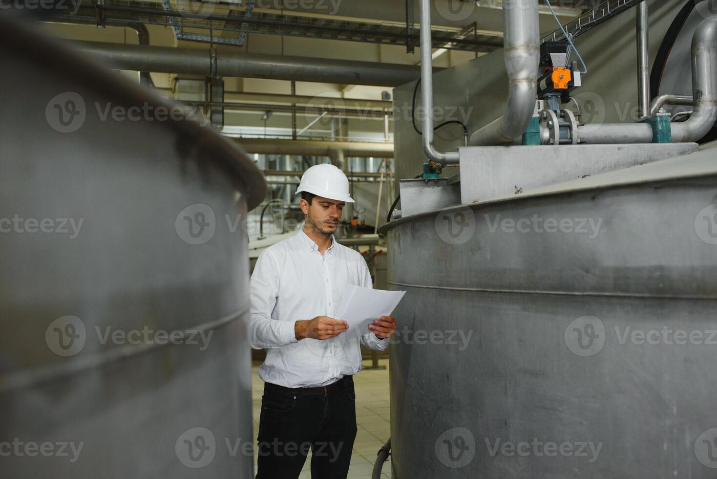 A young handsome employee of a modern factory in a white hard. In the background is a large shop for the production. photo