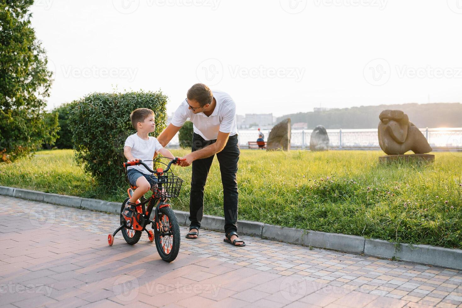 joven y contento padre enseña su joven hijo a paseo un bicicleta. el niño es contento . padre acecho hijo. del padre día foto