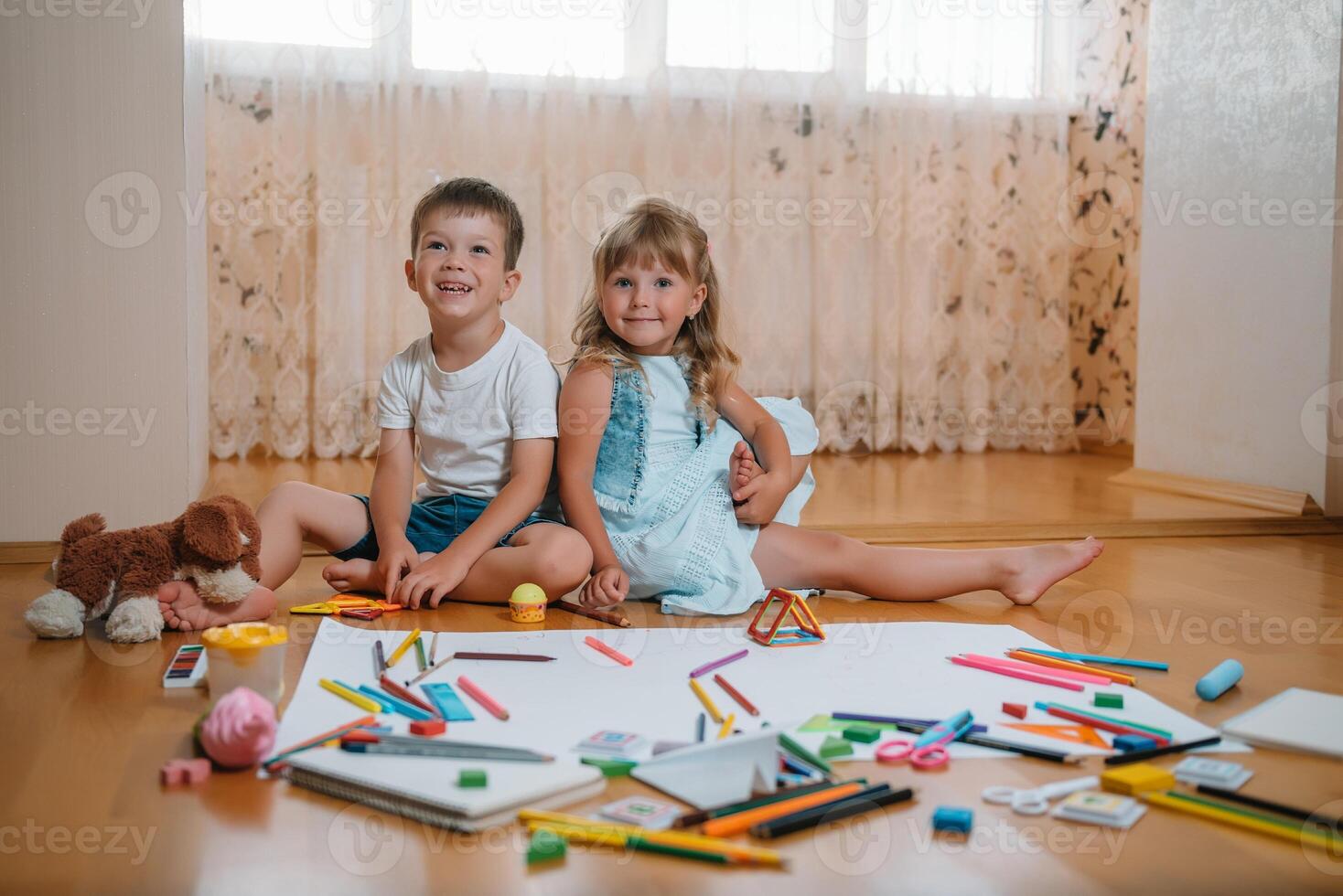 Kids drawing on floor on paper. Preschool boy and girl play on floor with educational toys - blocks, train, railroad, plane. Toys for preschool and kindergarten. Children at home or daycare photo