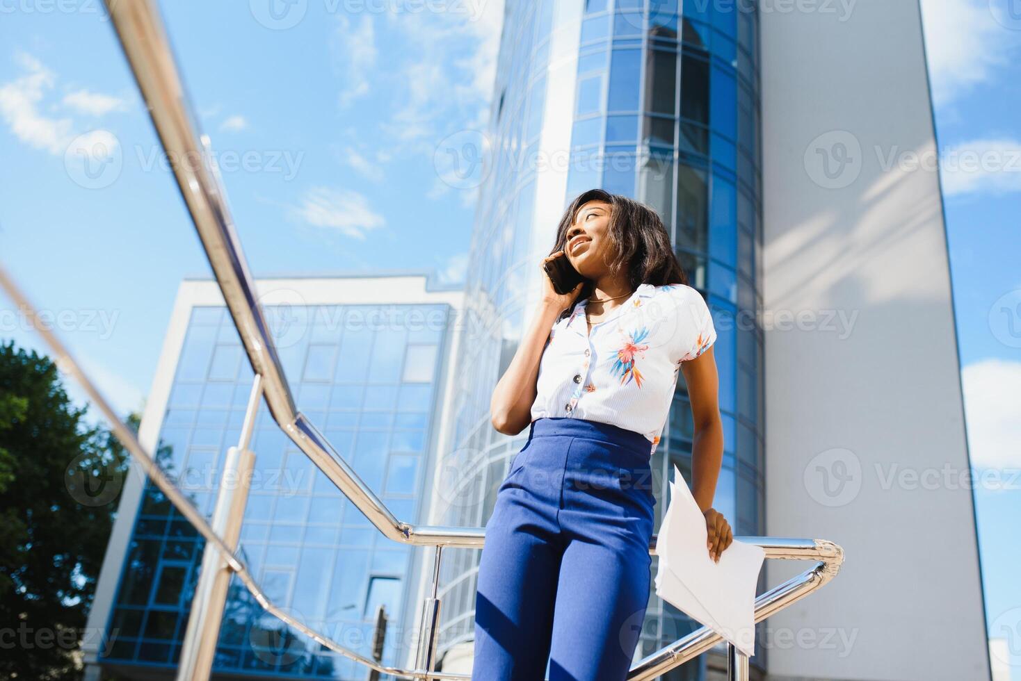 sonriente africano americano mujer de negocios utilizando móvil teléfono en calle en contra edificio foto