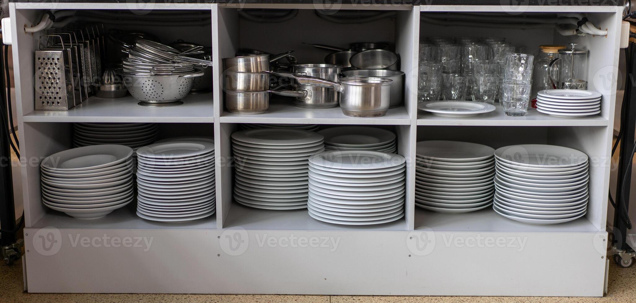 Stack white clean plates and other metal utensils  on the shelves in commercial restaurant. photo