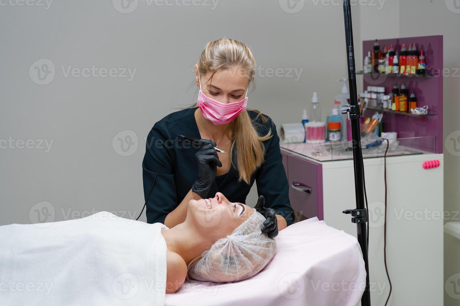 Cosmetology cabinet client lies on couch. Beautician applies marking on eyebrows. photo