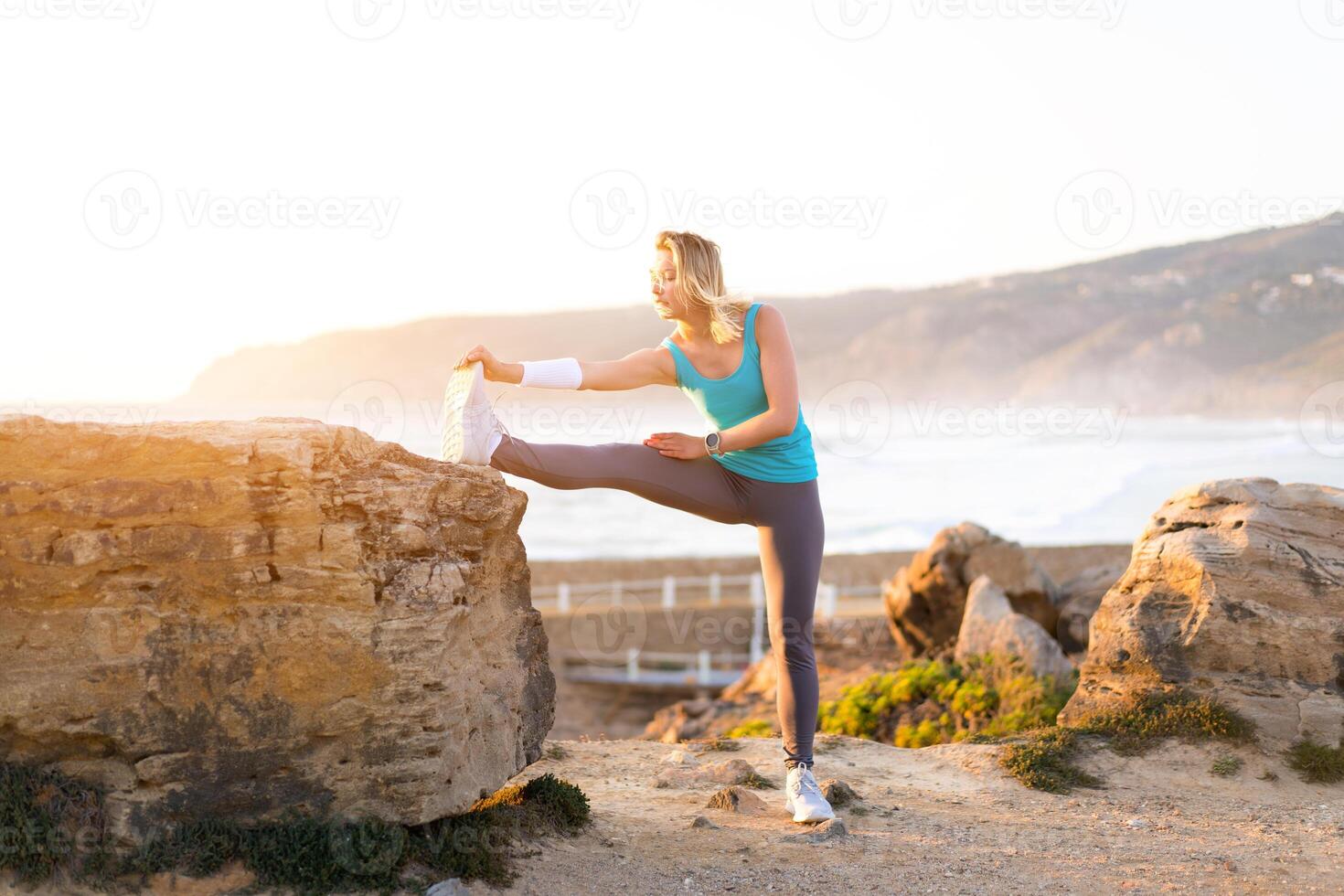 Flexible caucasian girl stretches legs after an intensive running workout. Athletic female middle age warming up before jogging workout outdoor photo