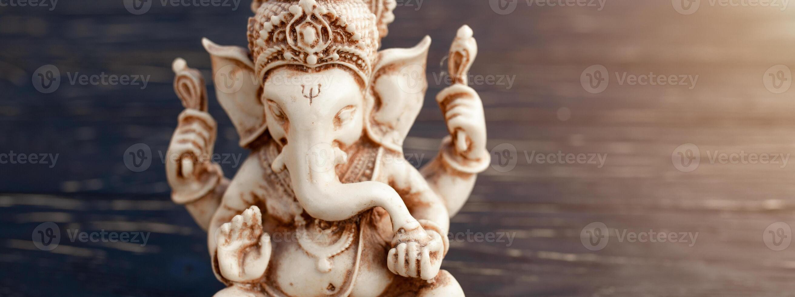 Hindu god Ganesh on black background. Statue on wooden table photo