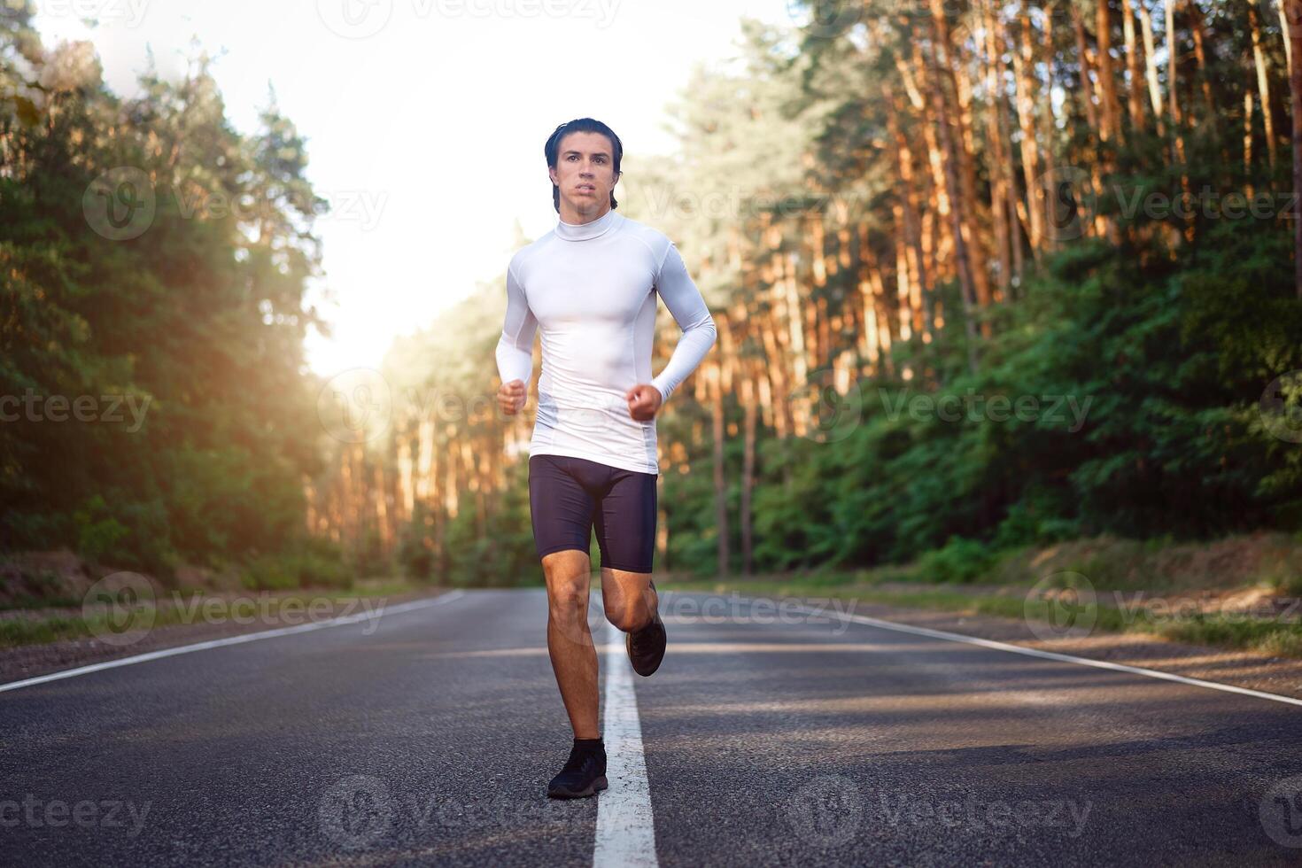 Caucasian middle age man athlete runs sunny summer day on asphalt road in the forest. photo
