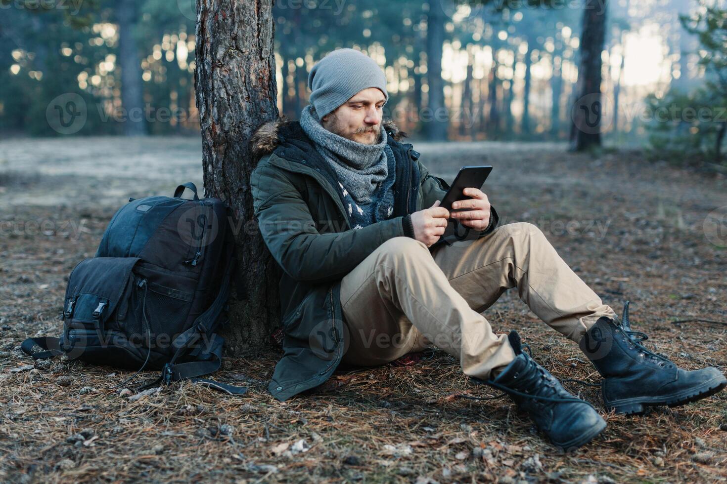 adult handsome Male traveler Sits On autumn pine forest Near tree, Holding At Tablet Recreation Resting Travel Destination Concept photo