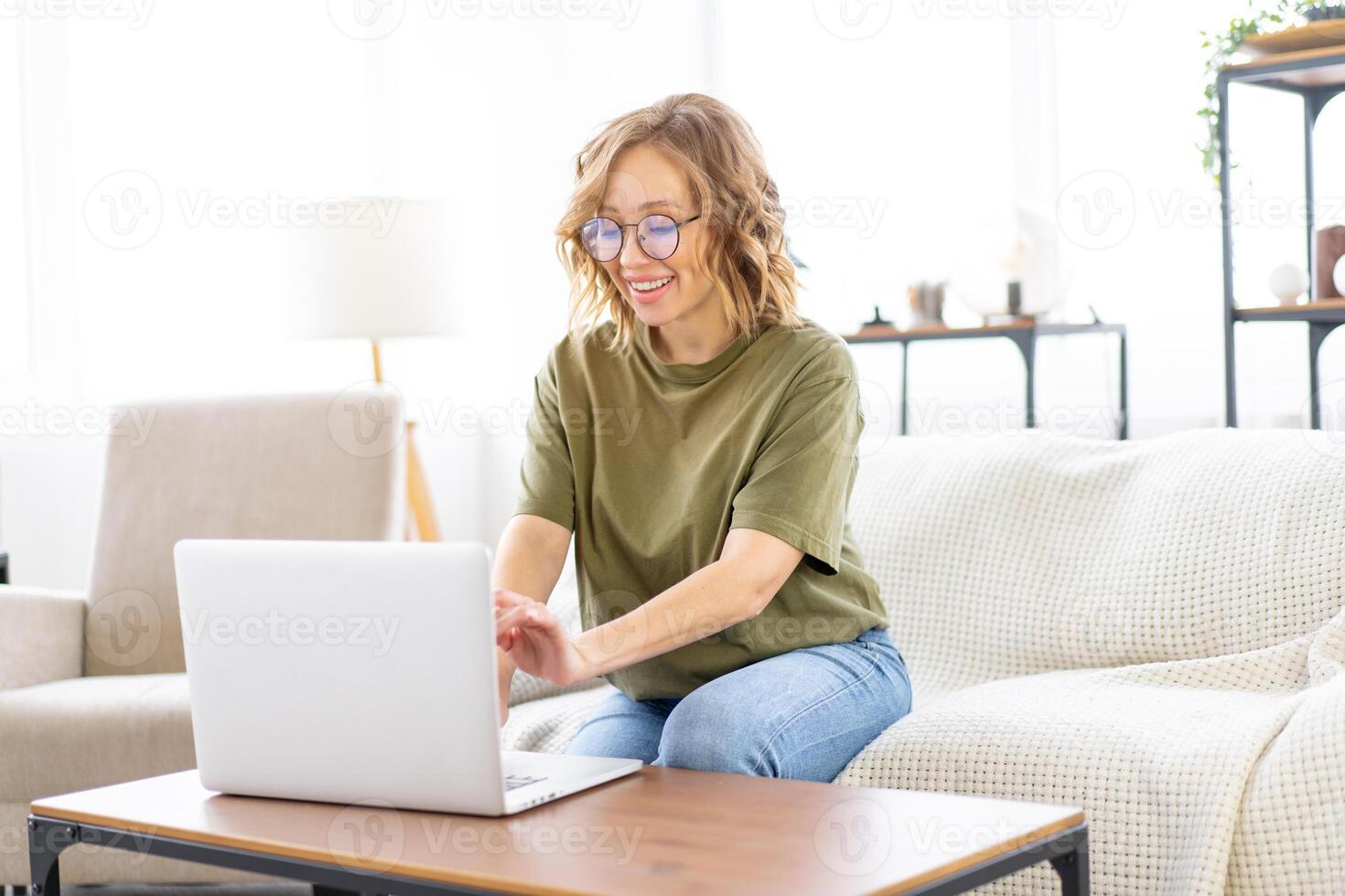 Woman glasses using laptop computer while sitting sofa with big window on background at home interior photo