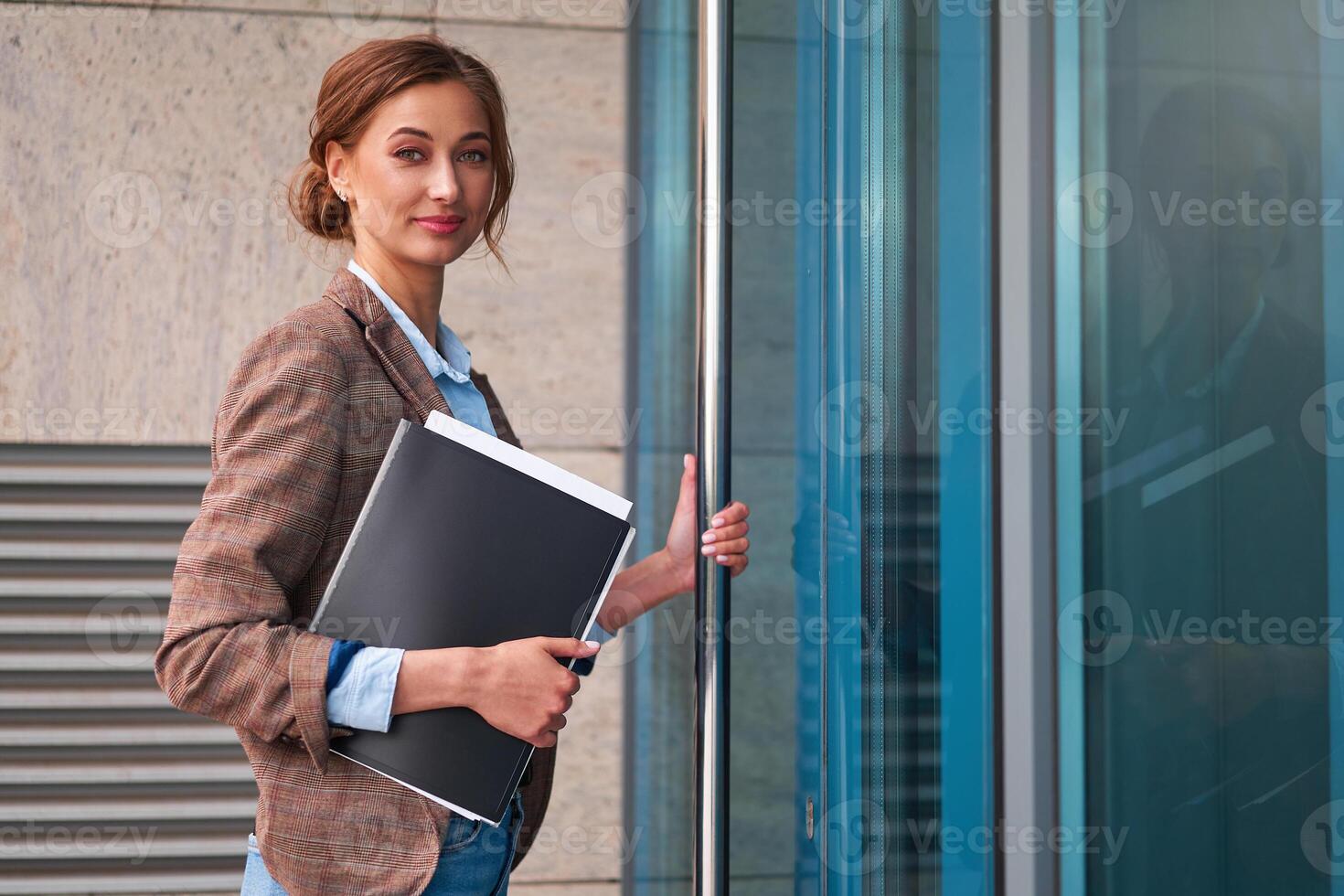 Business woman with a folder of documents in her hands opens the door of the business center and looks into the camera. Business concept. photo