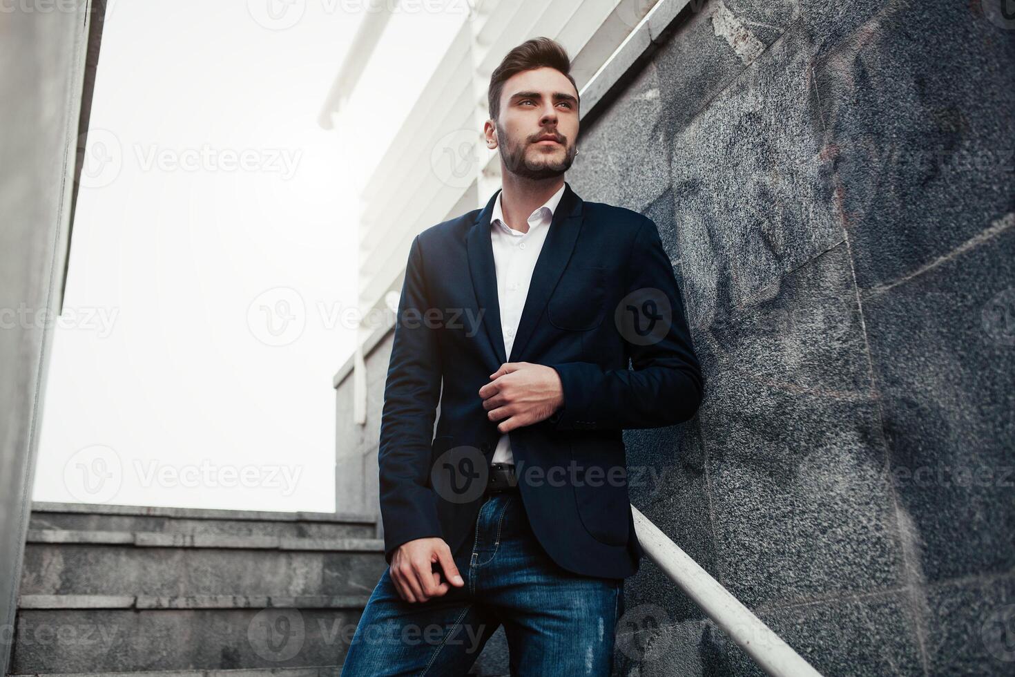 handsome young businessman with a beard and in a business suit standing on the street against the background of the office building photo