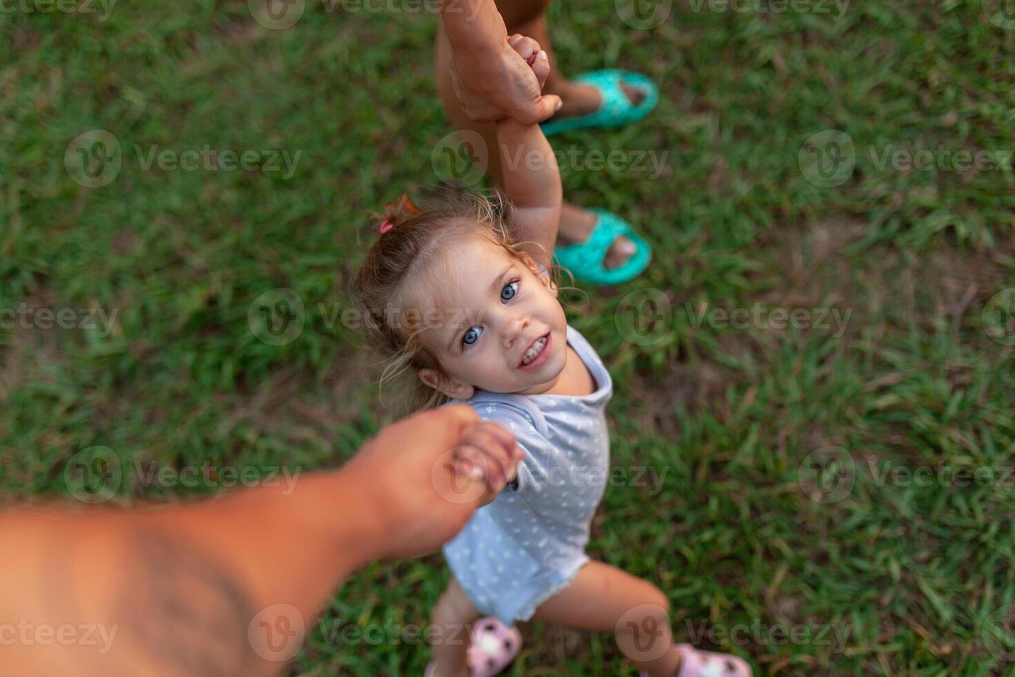 View from above of beautiful family, pretty mother, father and daughter, toddler, baby, looking up at the camera, on field, nature background. photo