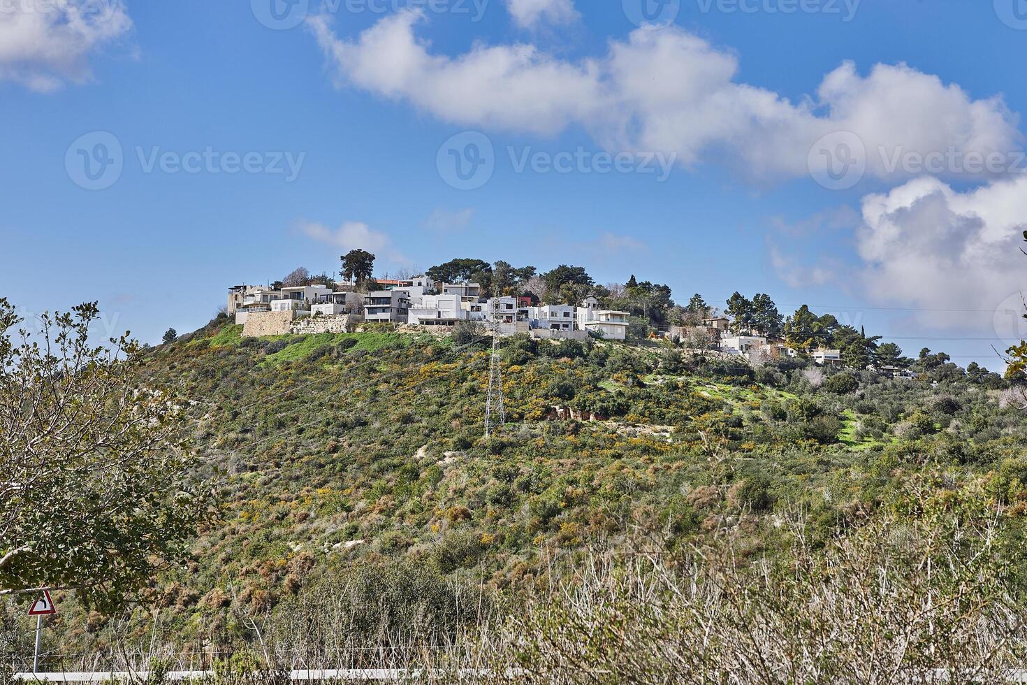 Rocky hill with a dirt road in front under a blue sky with white clouds and a modern villa on top photo