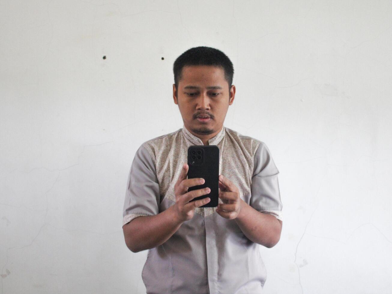 Adult Asian man texting on his mobile phone with  serious expression photo