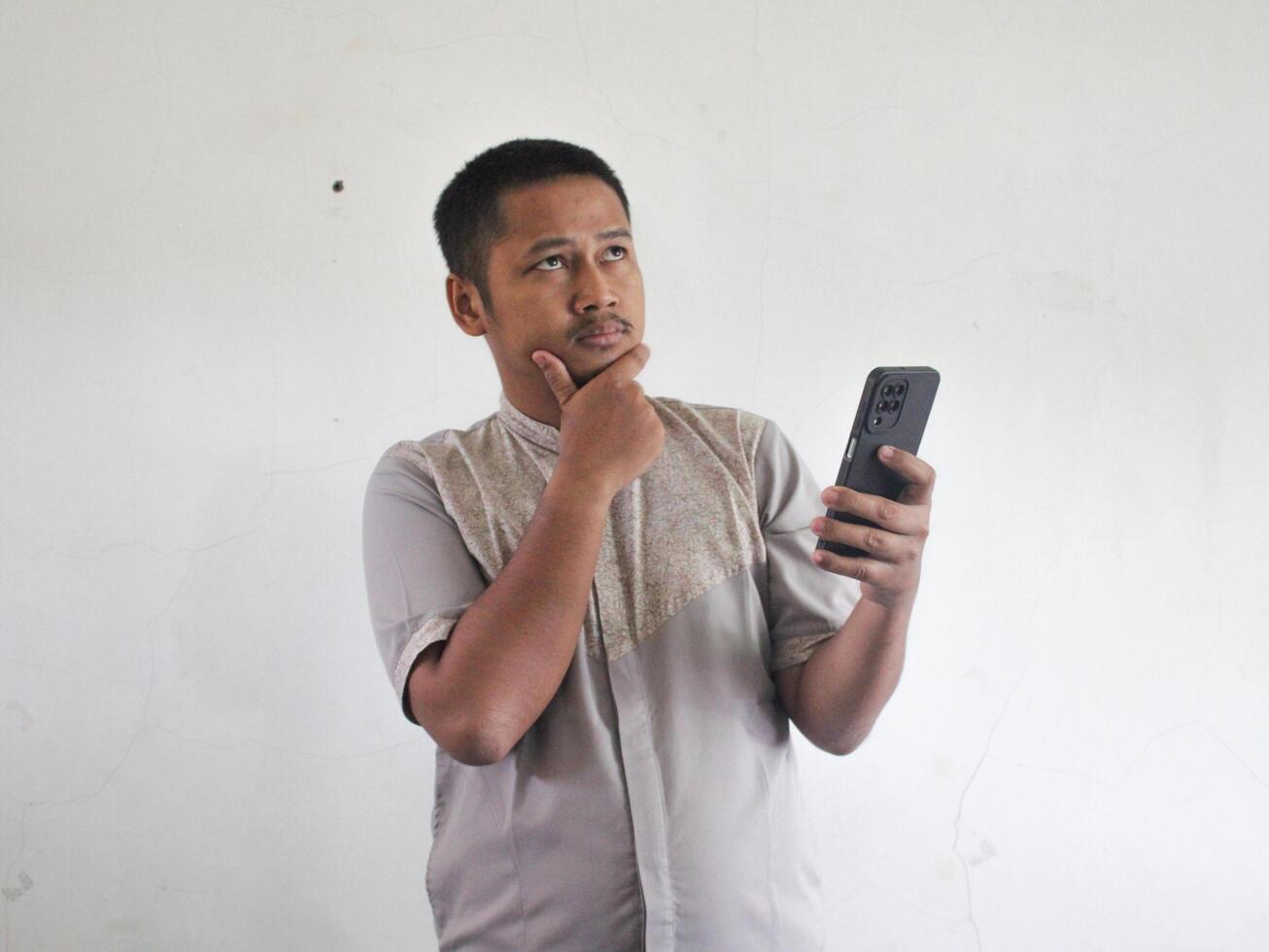 Asian man holding his mobile phone with serious expression photo