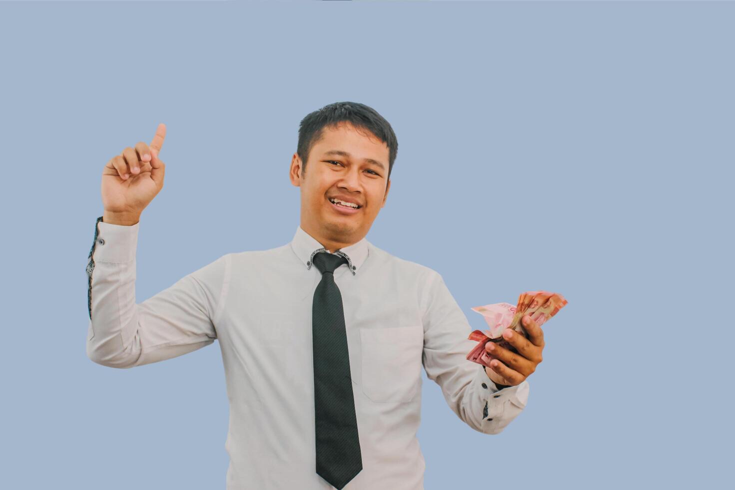 Adult Asian man smiling and pointing finger up while holding indonesian rupiah paper money photo