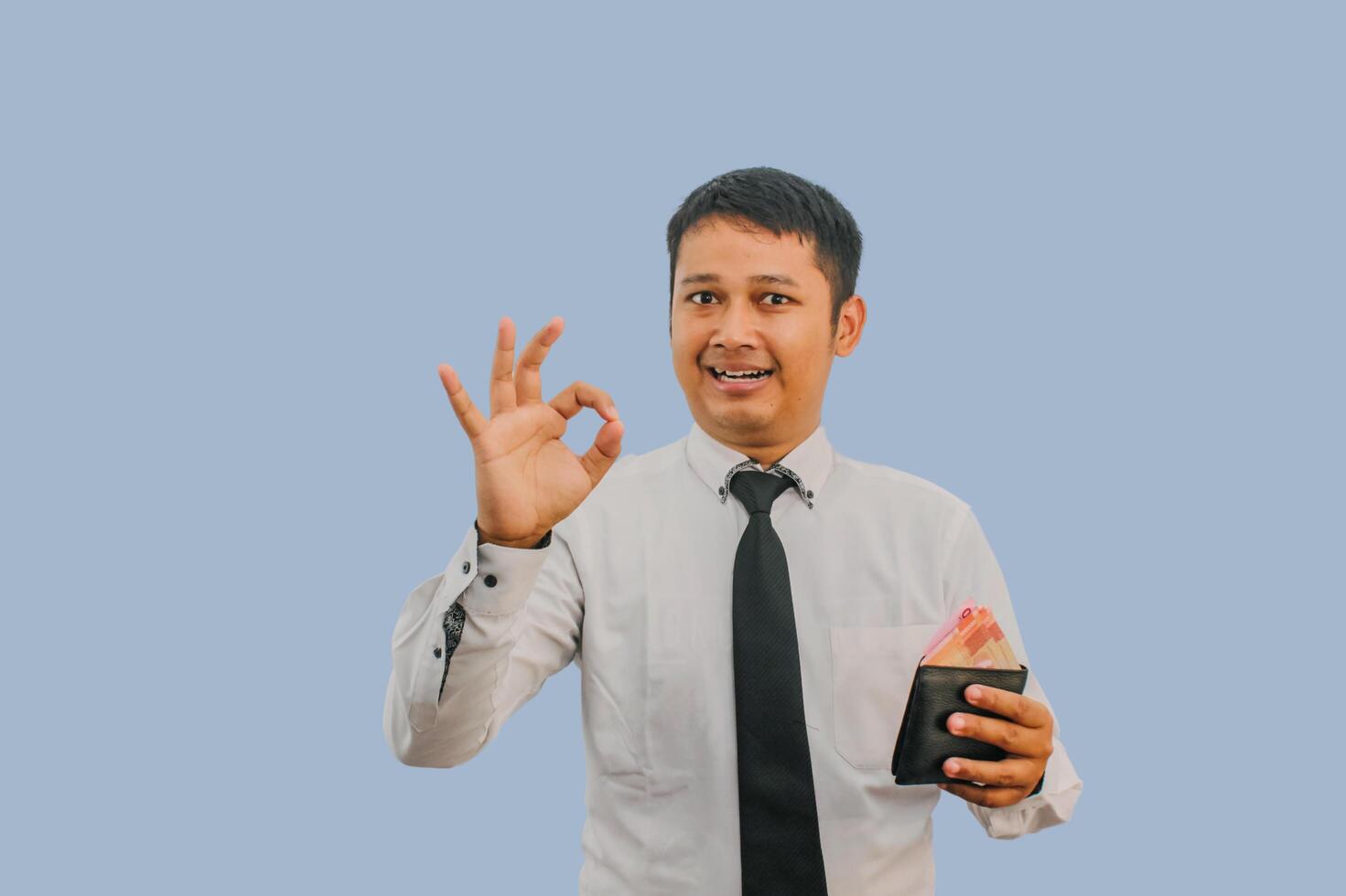 Adult Asian man smiling while holding wallet with money and give OK finger sign photo