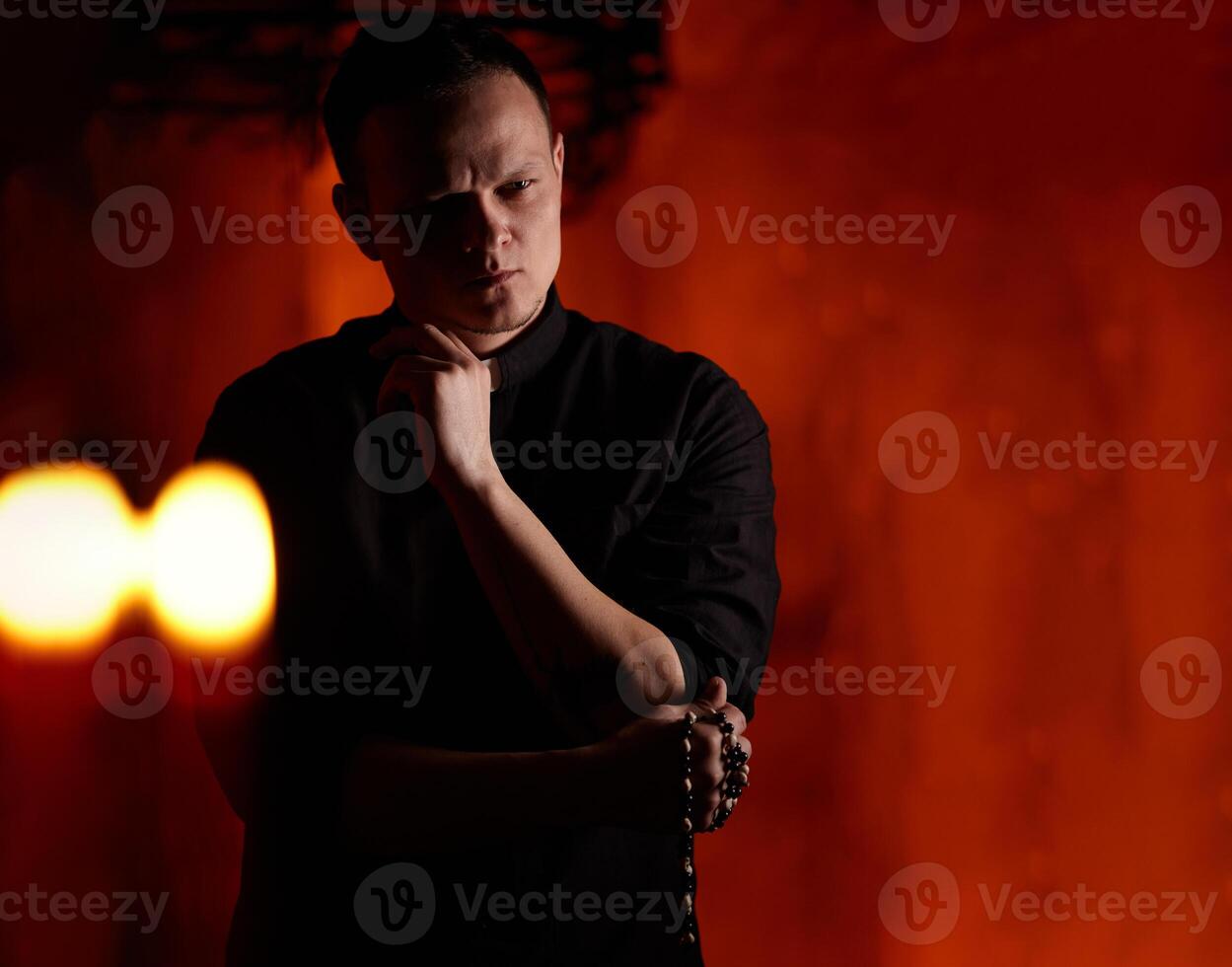 Young adult caucasian catholic priest on dark red background photo