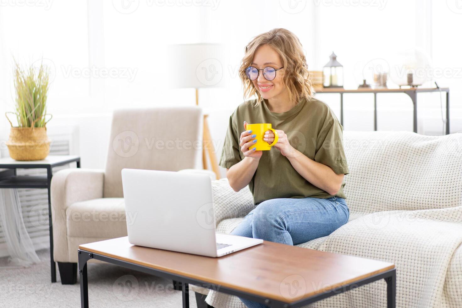 Woman glasses using laptop computer while sitting sofa with big window on background at home interior photo