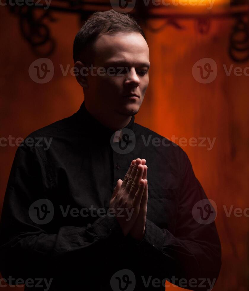 Portrait of handsome catholic priest or pastor with dog collar, dark red background. photo