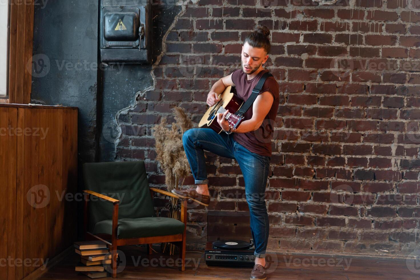 Man with acoustic guitar against brick wall playing music singing songs enjoy life Medium shoot photo