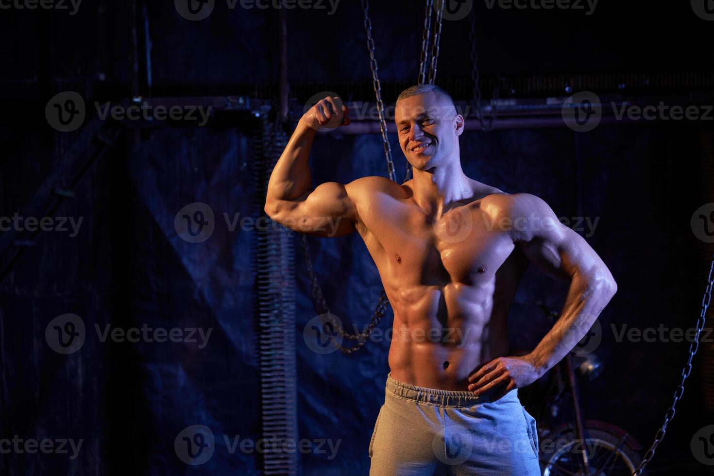 Young shirtless muscular man standing among metal chains, looking at camera, copy space photo