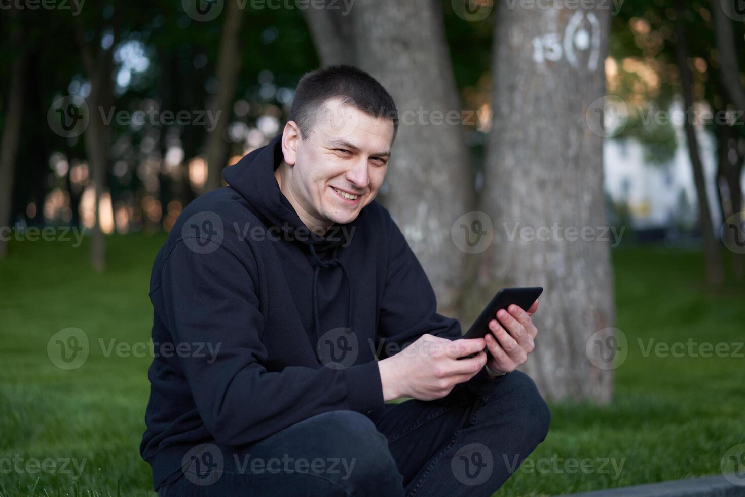 Man reading electronic book handsome guy read e-book tablet sitting public park summer day Caucasian male holding ebook in hand looking device screen photo