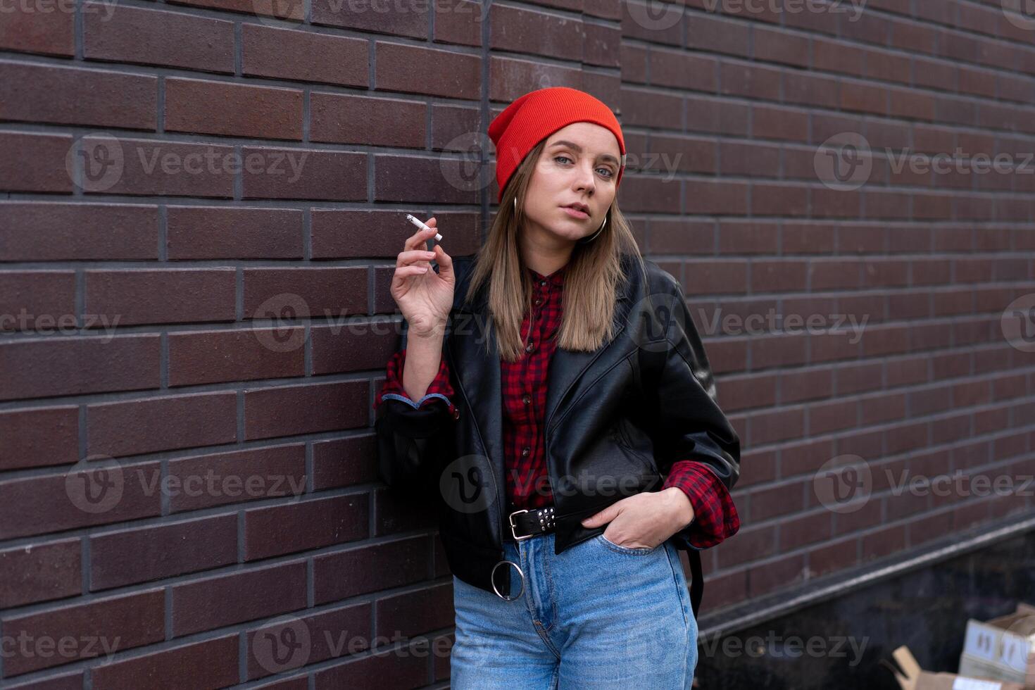 Beautiful young stylishly dressed Caucasian girl smokes cigarette on the street. photo