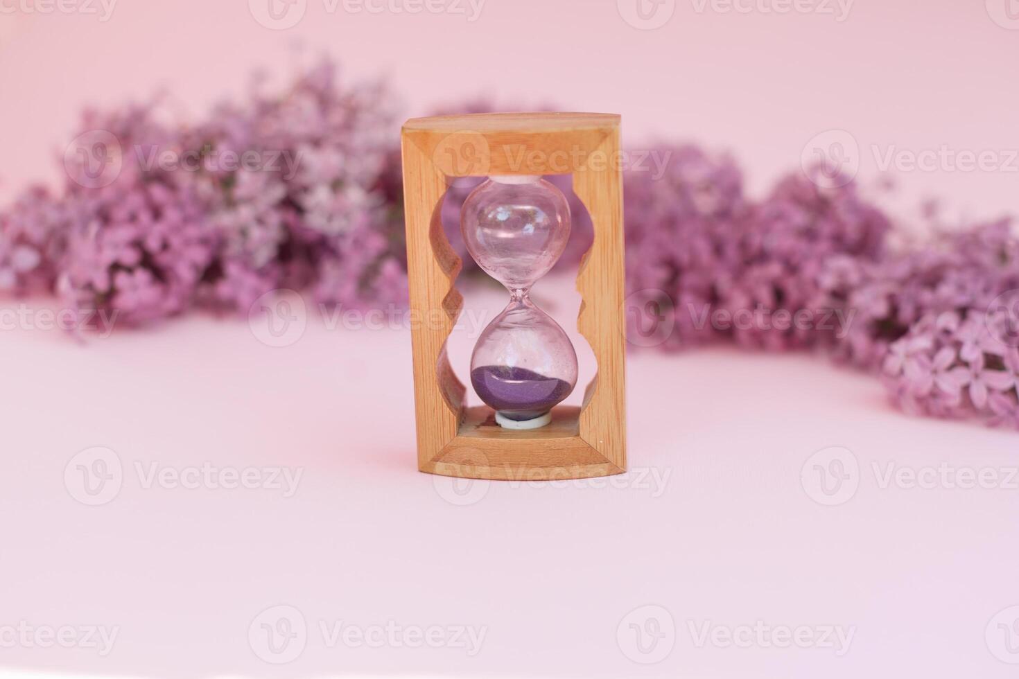 Sand running through the bulbs of an hourglass measuring the passing time in a countdown to a deadline, on a flower lilac spring background with copy space. photo