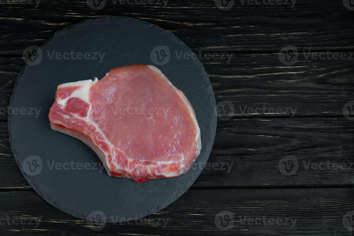 Top view of one pieces raw pork chop steaks on a black stone cutting board. photo