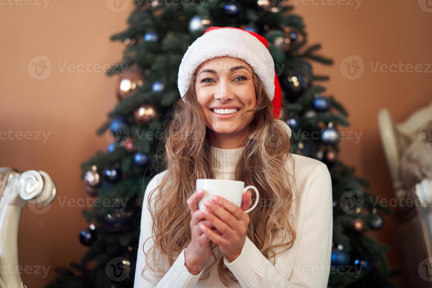 Christmas. Woman dressed white sweater Santa hat and jeans sitting on the floor near christmas tree with present box photo