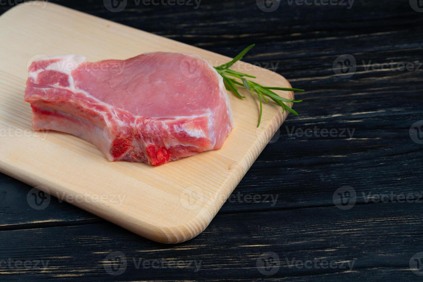 Top view of one pieces raw pork chop steaks with rosemary on a cutting board. photo