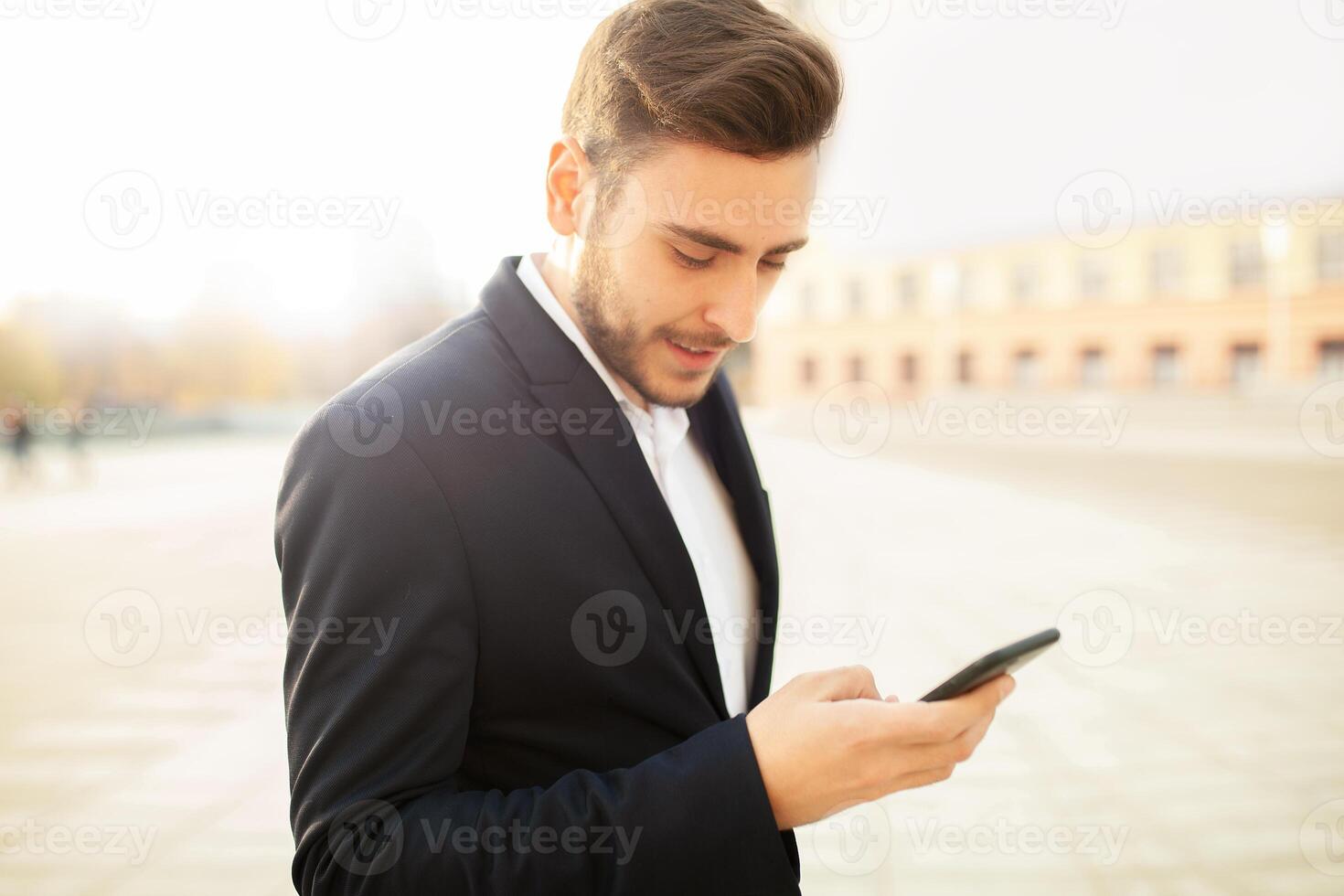 Millennial businessman looks into the screen of his mobile phone. Close-up portrait. Young successful, stylish business man walks on a city street, watching social networks in his smartphone photo