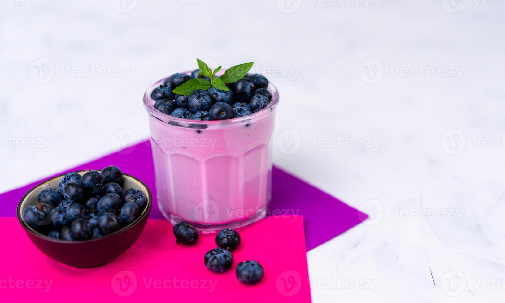 Tasty fresh blueberry yoghurt shake dessert in glass standing on white table purple napkin background. photo