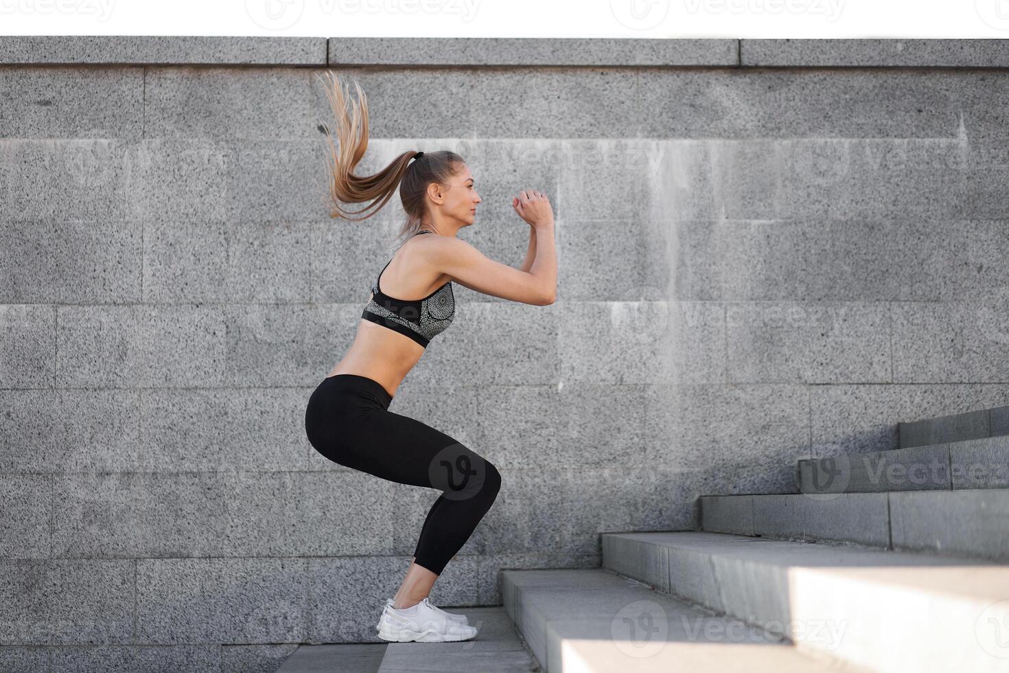 urbano deportivo mujer capacitación. hembra atleta haciendo ponerse en cuclillas saltos en urbano escaleras. foto