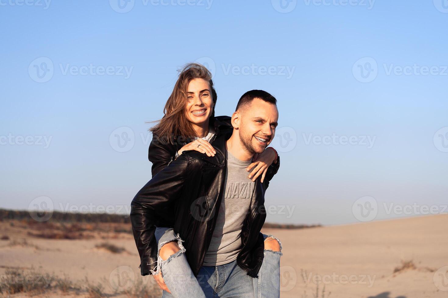 Happy and cute adorable adult couple of millennial hipsters, man with woman girlfriend on piggy back, have fun play photo