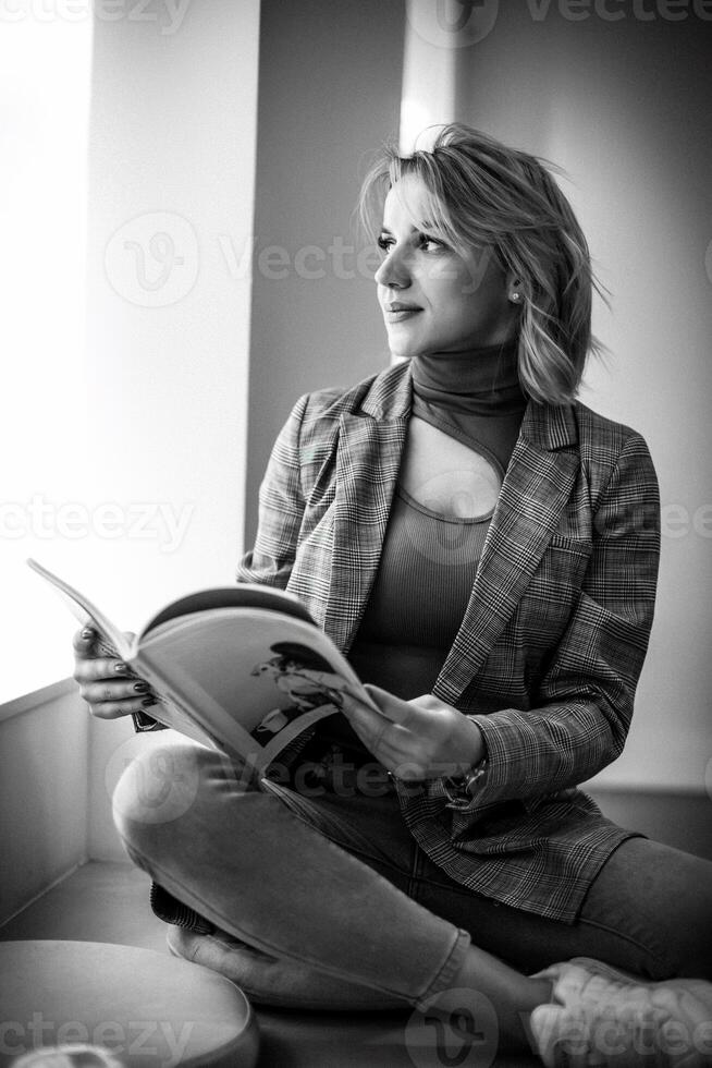 Woman Reading Magazine on Floor - Casual Relaxation with Printed Media - Young Lady Enjoying Leisure Time in Plaid Jacket and Jeans, Cozy Lifestyle Concept. photo