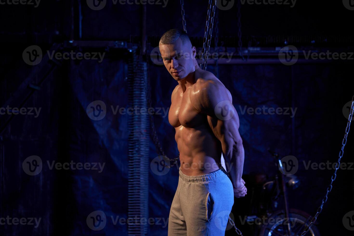 Young shirtless muscular man standing among metal chains, looking at camera, copy space photo