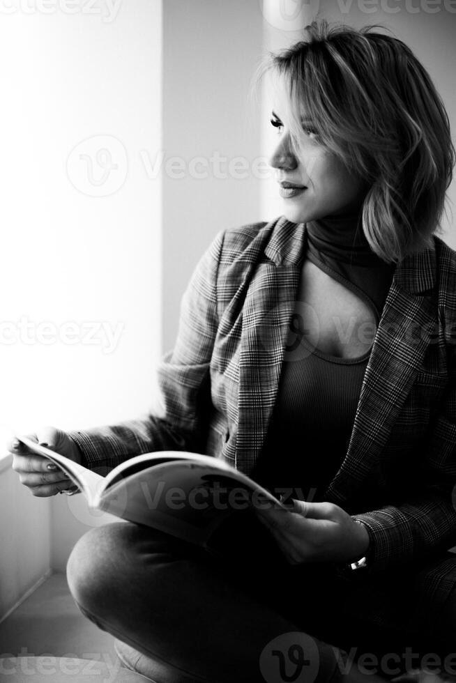 Stylish Woman in Plaid Jacket Relaxing with Magazine - Fashionable Female Enjoying Leisure Time in Chair - Cozy Reading Session with Chic Attire, Lifestyle Concept. photo