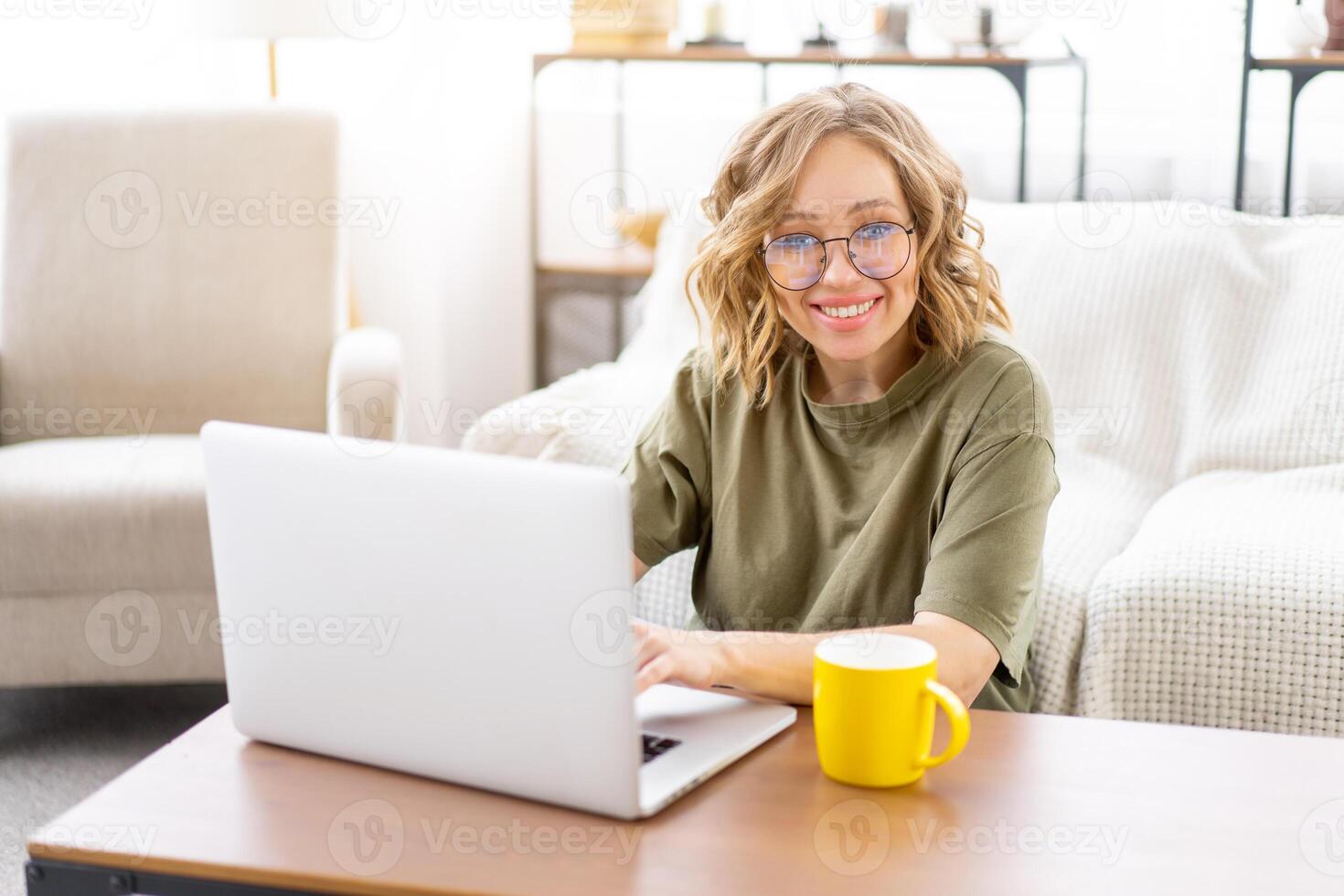 Woman glasses using laptop computer while sitting near sofa with big window on background at home interior photo