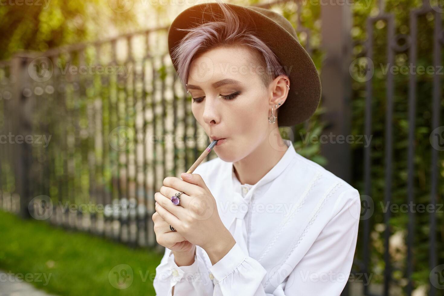 Beautiful informal girl with purple short hair and in a fashionable hat smokes a cigarette photo