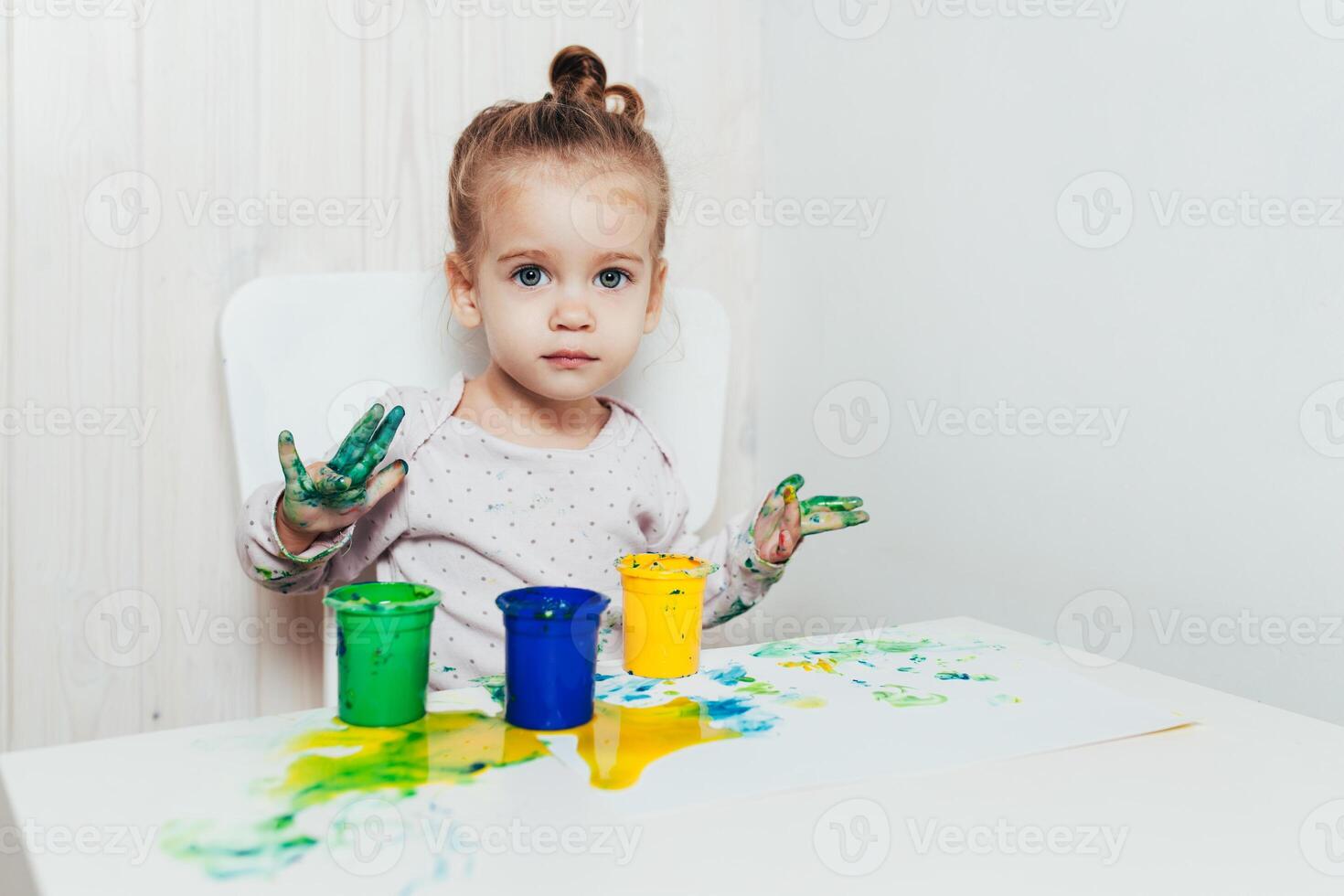 hermosa pequeño niña sorteos con dedo pinturas en un blanco sábana de papel. creativo niño desarrollo en jardín de infancia o gratis hora a hogar foto