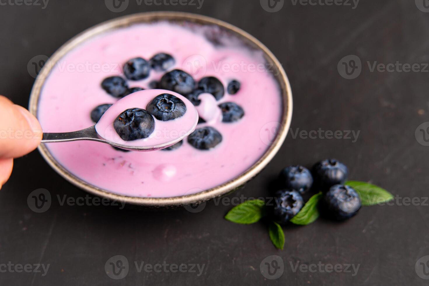 Tasty fresh blueberry yoghurt shake dessert in ceramic bowl standing on black dark table background. photo