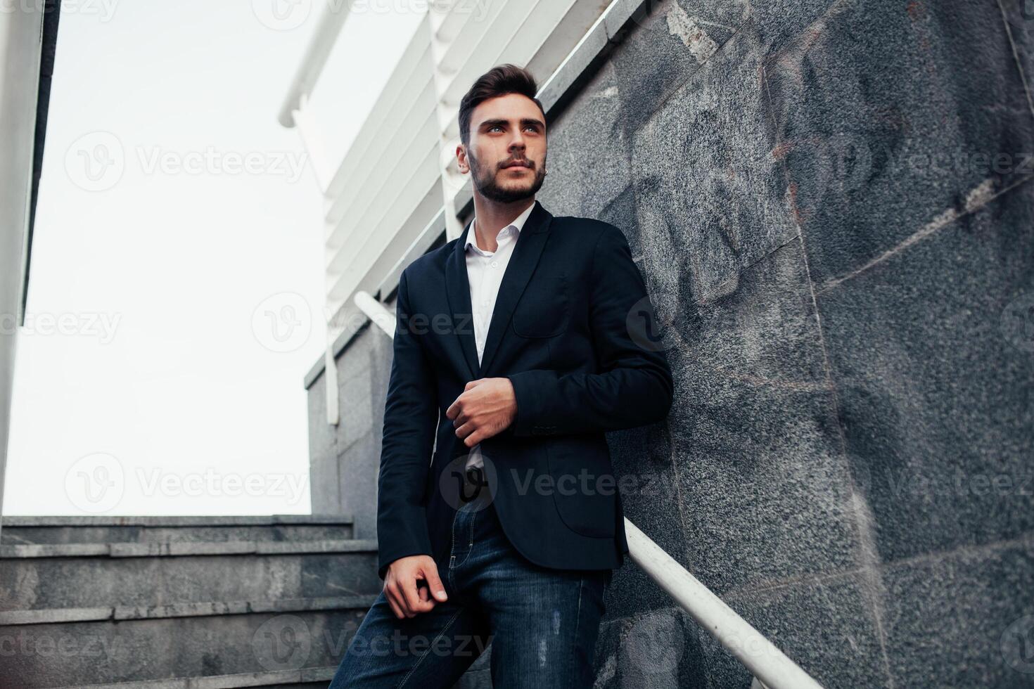 Young stylish businessman man with a beard in a fashionable suit and jeans. Modern image of business youth. It stands on the background of marble walls photo