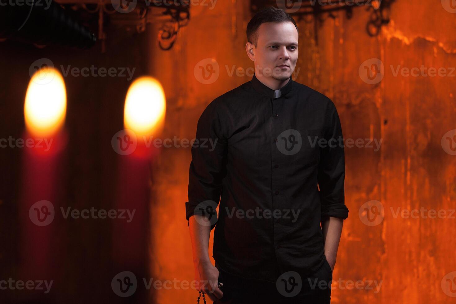 Portrait of handsome catholic priest or pastor with dog collar, dark red background. photo