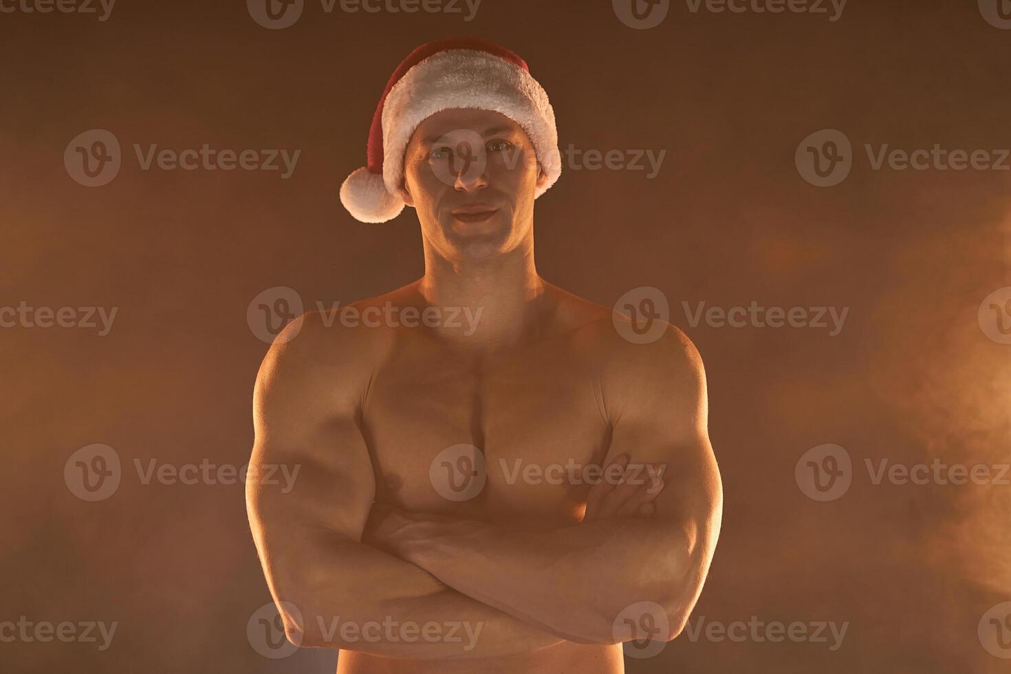 retrato de muscular hombre vistiendo Navidad Papa Noel sombrero, doblada manos en ahumado antecedentes foto