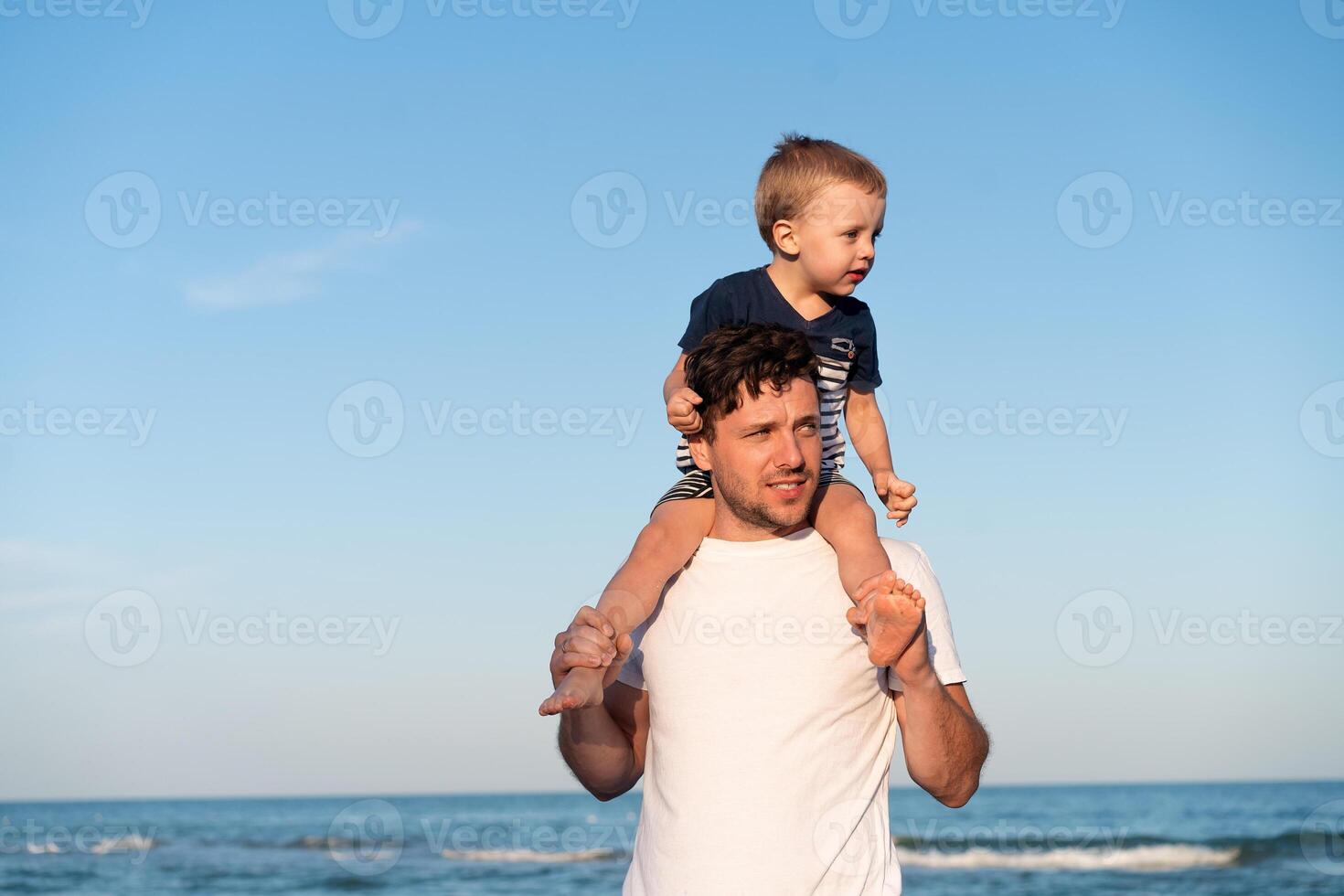 Young Caucasian dad with little son walk warm summer day along the sea coast. Summer family vacation concept. Friendship father and son. photo